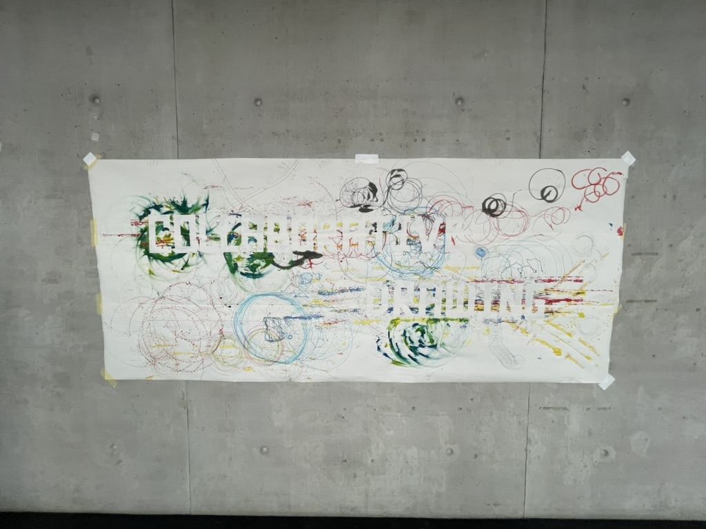 Large paper banner on a concrete wall with colourful robot traces and the white letters Collaborative Drawing