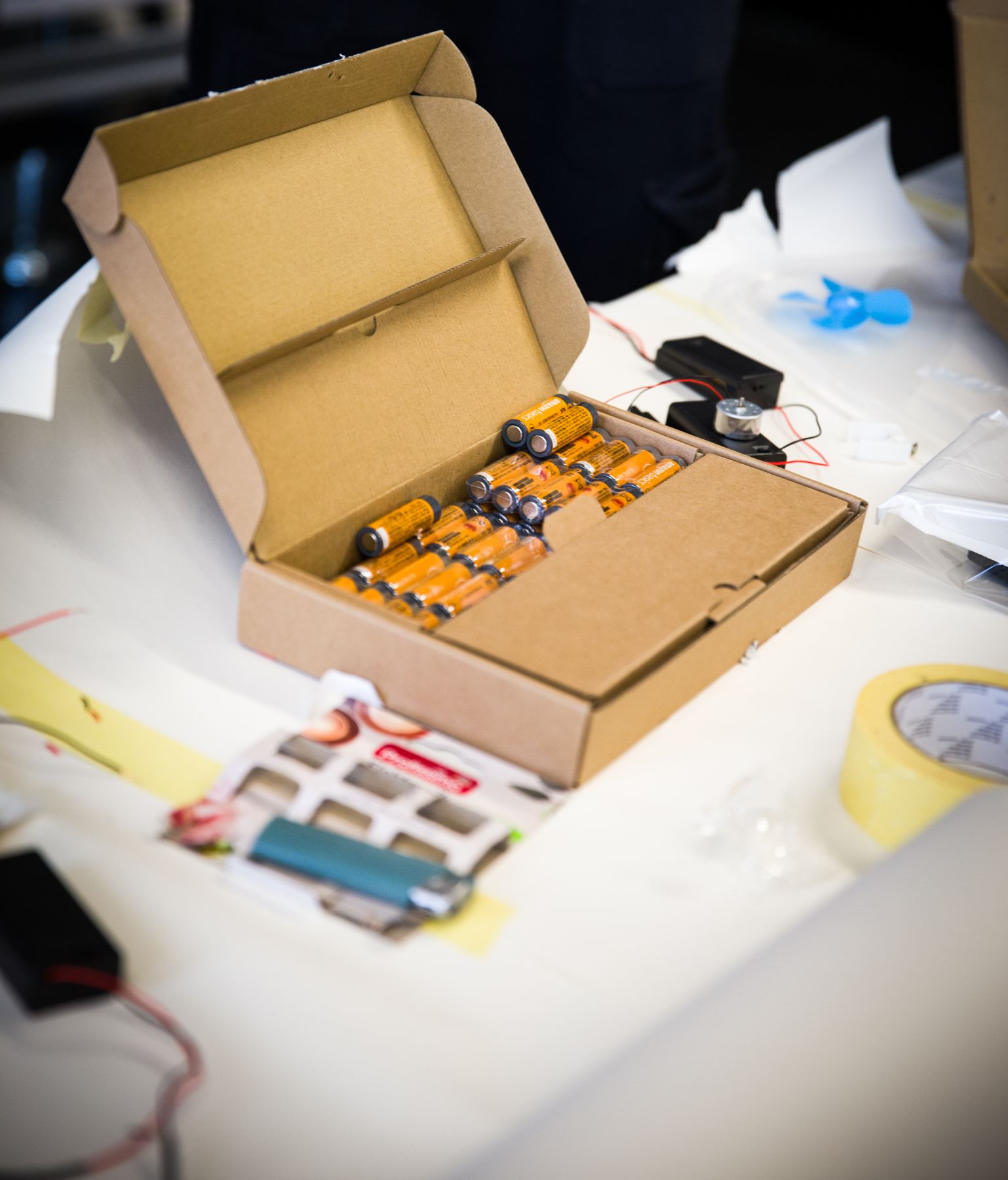 A cardboard box full of AA batteries next to a battery holder and a small fan