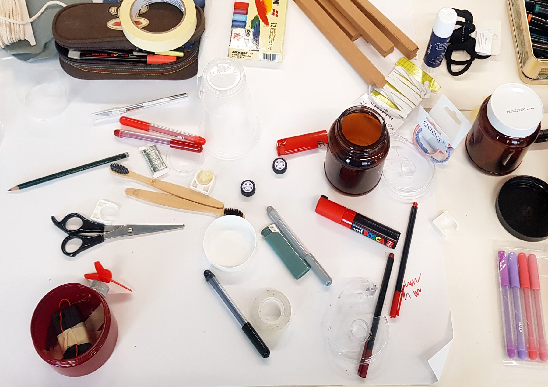 Table seen from above with a red jar, pens, toothbrushes, tape, scissors and jars
