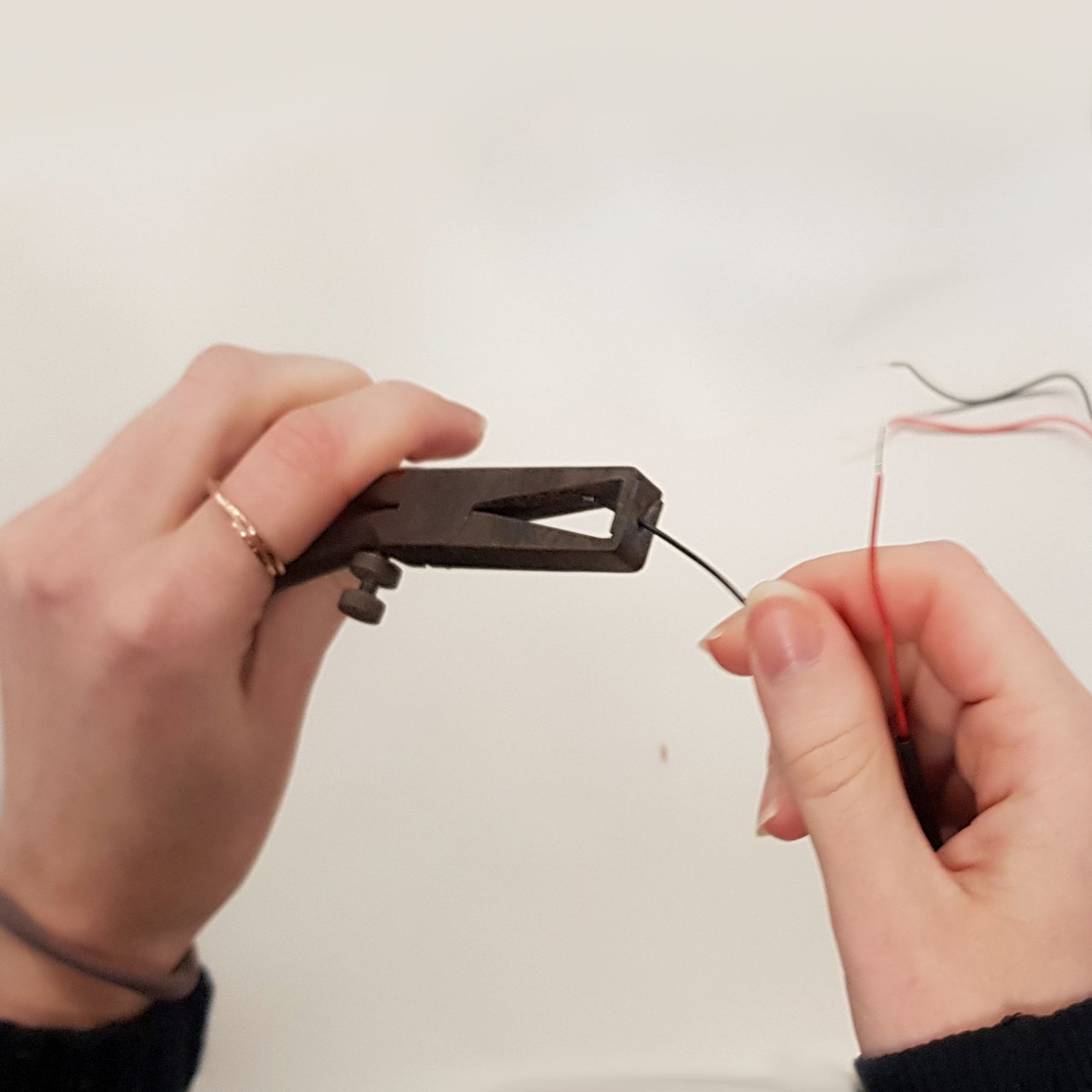 Hands stripping a thin red wire with pliers