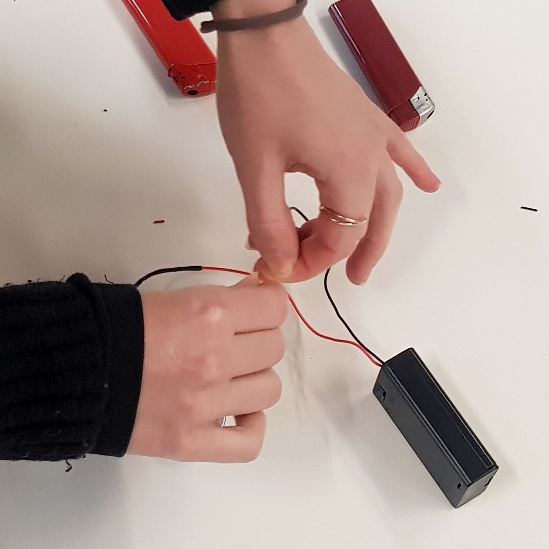 Hands twisting wires to a black battery holder