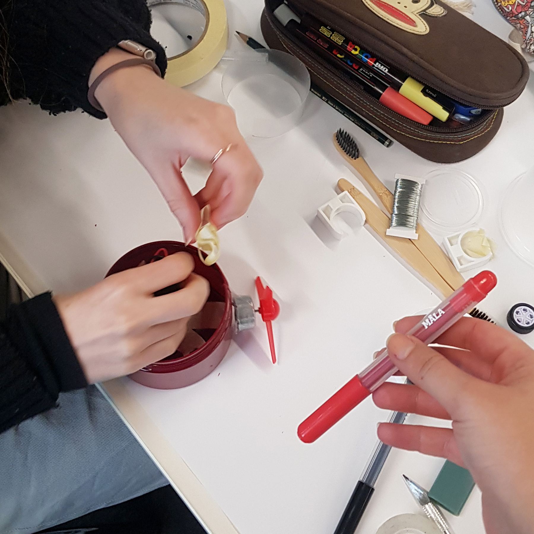 Hands placing parts inside a red jar with a fan on the side