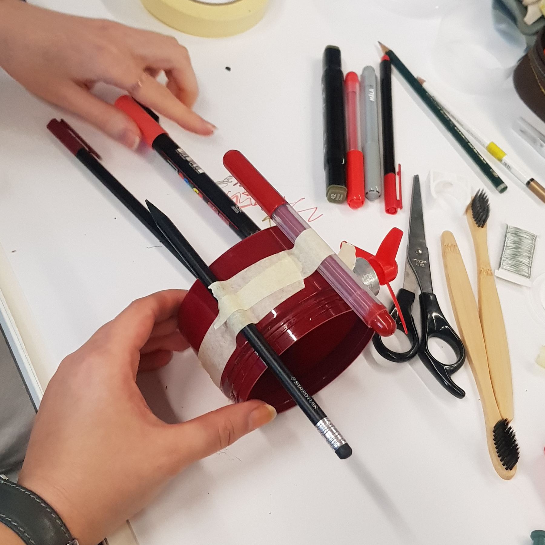 Hands taping pens to a red jar
