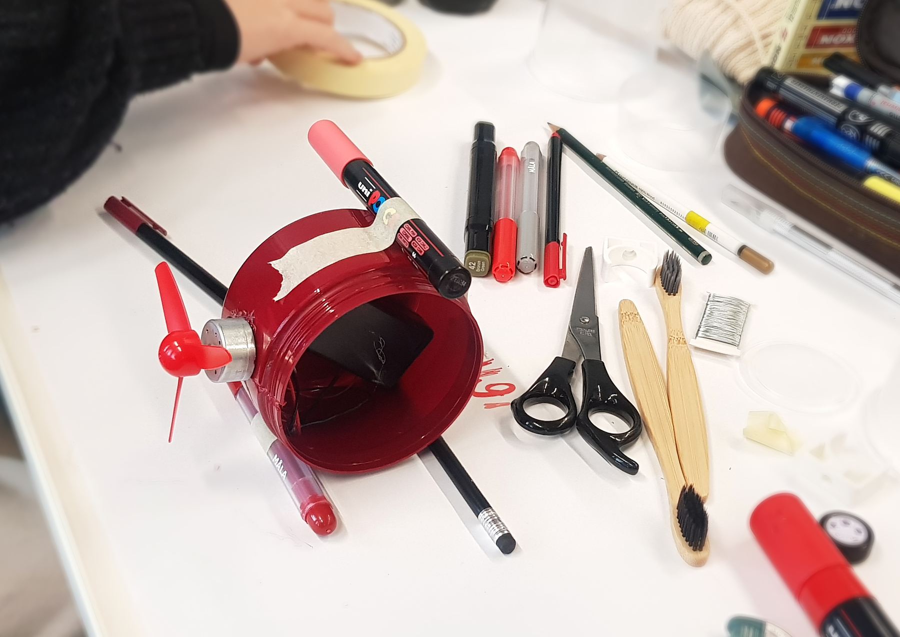 Red jar with fan, motor and pens taped on, lying on its side
