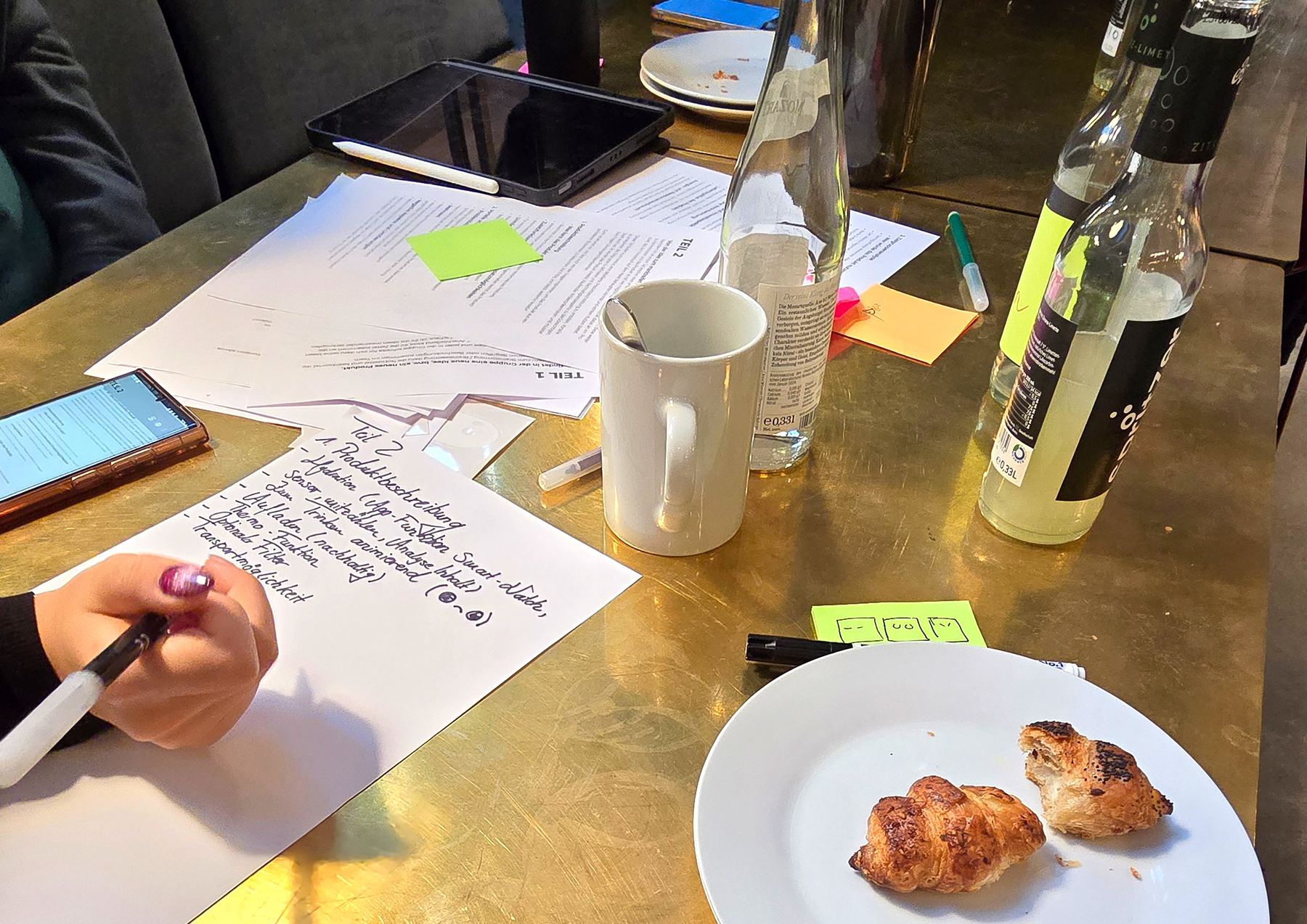 Hand writing notes on paper next to a plate of croissants