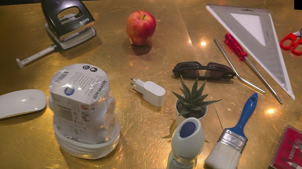 Objects on the table: hole punch, apple, computer mouse, power strip, plant, tools